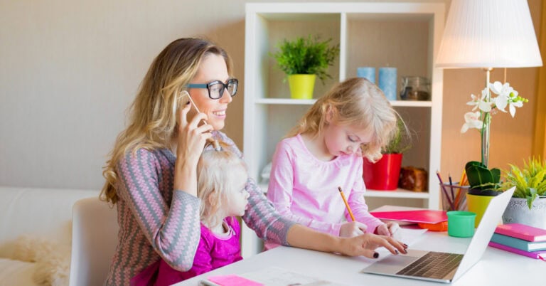 mother on phone, working on computer, with two children nearby