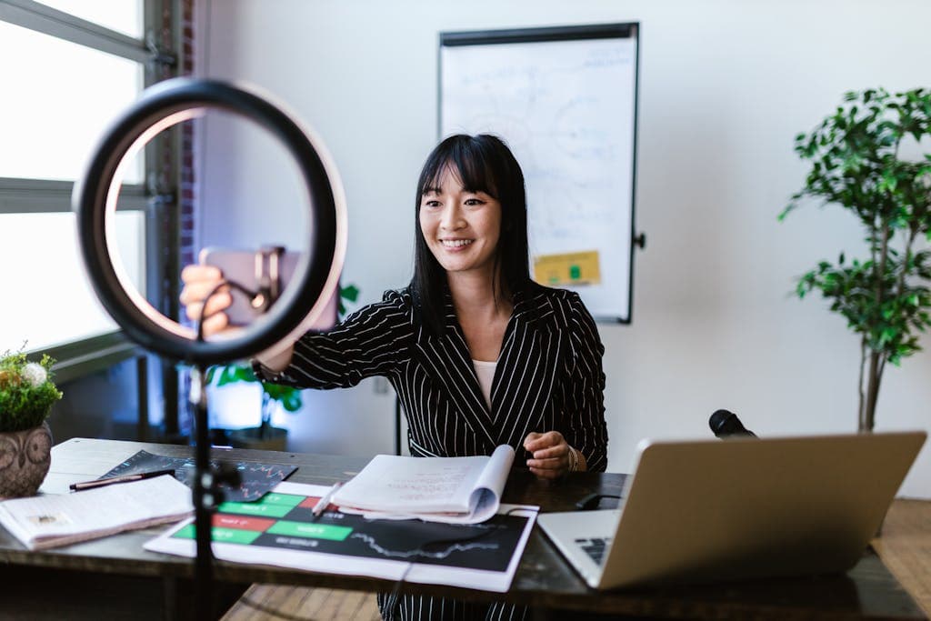 A woman vlogger uses her smartphone to create content in a professional office setting.